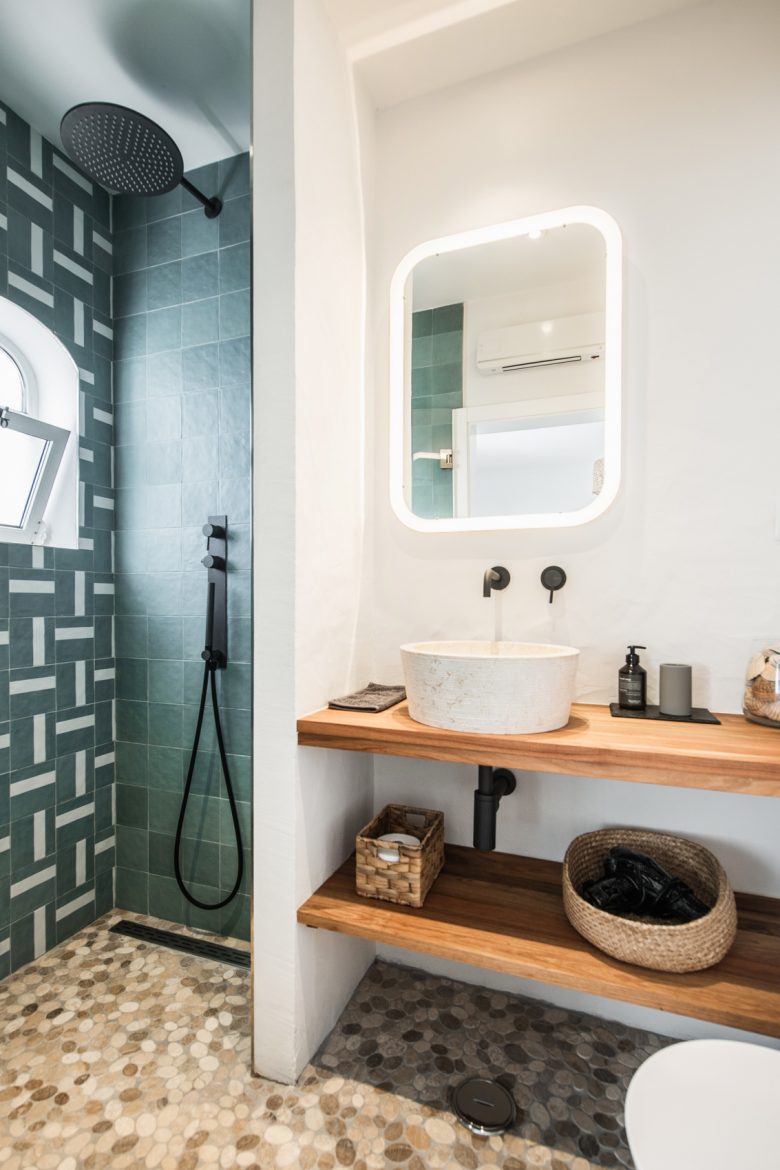 Casa de banho elegante na CASA KALU com azulejos azuis modernos, chuveiro de efeito chuva e lavatório de pedra natural sobre uma consola de madeira no Algarve