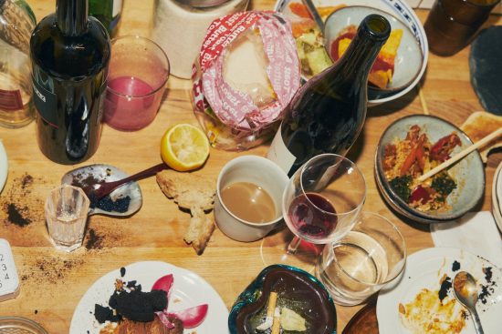Tisch mit Essensresten und leeren Weinflaschen